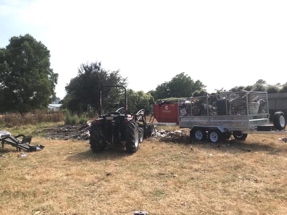 Junk Masters tractor towing a cage trailer full of inorganic waste in a paddock